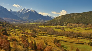 Wide valley with a mixture of yellow and green fields surrounded by mountains, autumn foliage,