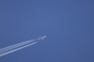 Boeing 747 jumbo jet aircraft flying across a blue sky with a vapour trail or contrail behind,