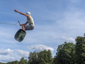 Young man jumping and flying with wakeboard, water sports and water skiing in the wakepark