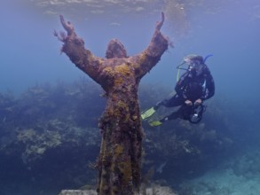 Diver with camera looking at an underwater statue of Jesus Christ (Christ of the Abyss), dive site