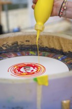 Hand holding a yellow bottle and dripping colour into a spiral pattern, Nagold, Black Forest,