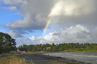 Beach landscape with rainbow and clouds over the sea and green vegetation in the background,