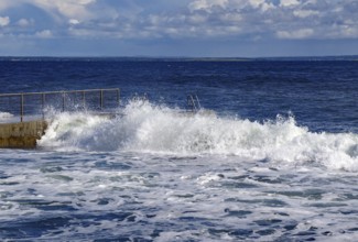 Waves crashing against a railing by the sea under a slightly cloudy blue sky, Tönsberg, Oslofjord,