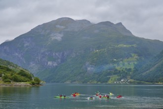 Several kayakers in a fjord surrounded by forested mountains and clouds, Geiranger, Geiranger