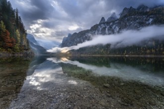 The Vordere Gosausee in autumn with a view of the Gosaukamm on the right. The Dachstein in clouds