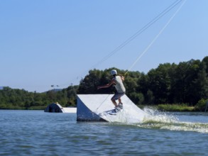 Young man jumping with wakeboard over jump into the lake, water sports, water skiing in wakepark,