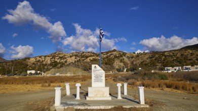 Monument with Greek flag in front of a clear blue sky and mountain landscape in the background,