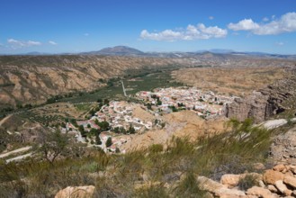 A village with white houses and red roofs, nestled in a dry, mountainous desert landscape under a