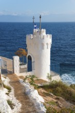 White tower on the coast with a Greek flag surrounded by the blue sea, Church of Agios Nikolaos