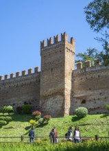 People walk in front of a tower on the defense wall of the medieval Gradara castle, Marche region,