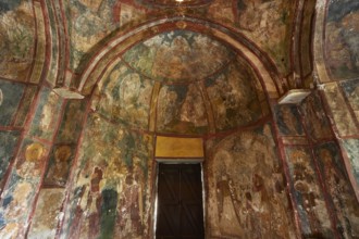 A church interior with frescoes on the walls, religious art and a large wooden door, Byzantine