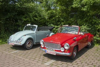 Two classic convertibles, one red and one light blue, parked next to each other on a paved car