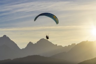 Paraglider over mountain silhouette at sunset with golden rays of light, Schwangau, Ostallgäu,