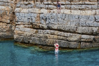 Palatia Beach, Palatia, A person jumps from a rocky cliff into the turquoise water, another person