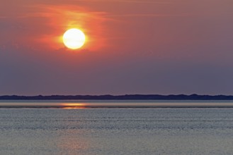 Sunset over the North Sea at low tide, the outline of the island of Juist on the horizon,