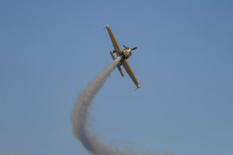 Golden stunt aerobatic plane performing stunts in blue sky with smoke trail. Concept of speed,