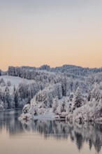 Dawn and sunrise at the wintry Forggensee in a snow-covered winter landscape in the foothills of