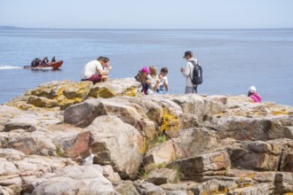 People on rocks by the sea with speedboat in the background in Gudhjem, Bornholm, Baltic Sea,