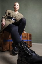 Close-up of a woman in stylish clothes on a wooden box with green background, photo shoot