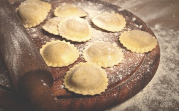 Fresh raw, uncooked ravioli, on a cutting board, with a rolling pin for dough, wooden background,