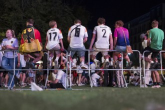 Fans with shirts of the German national team sit on barriers at the fan zone at the Brandenburg Tor