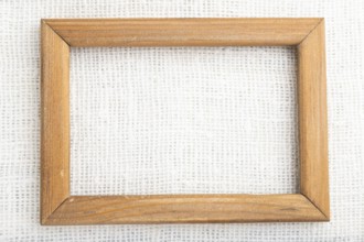 Wooden frame on smooth white linen tissue. Top view, flat lay, natural textile background and