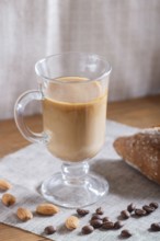 Glass cup of coffee with cream and bun on a wooden background and linen textile. close up