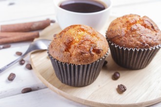 Two carrot muffins with cup of coffee on wooden kitchen board on white wooden background with