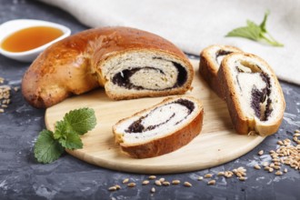 Homemade yeast rolls with poppy seeds and honey on a wooden kitchen board on a black concrete