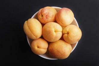 Fresh orange apricots in white bowl on black background. top view, flat lay, close up