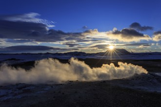 Hot springs and geothermal area in front of mountain landscape in winter, sunbeams, cloudy mood,