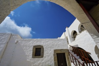 View from below of white buildings and a staircase under an arch in the Greek monastery, Inside the