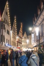 A lively street with half-timbered houses at night, illuminated by Christmas lights. Festive and