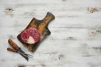 A raw beef steak on a wooden cutting board. Butcher knife and fork are placed below the cutting