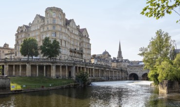 Large historic building and riverside church with clear skies, Bath