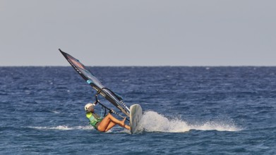 Person in green t-shirt balancing on a wave with a windsurfing board, windsurfer, Meltemi