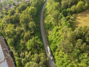 Train on rails through a wooded landscape with neighbouring houses, track construction, rail