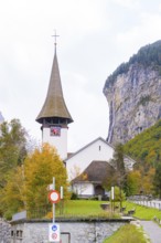 Church with pointed tower in front of rock face and waterfall in an autumn landscape,