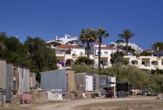 Corrugated iron huts, dwellings of labourers, behind them villas, holiday homes, contrast, poor,