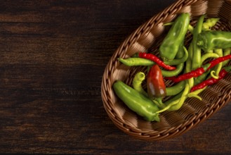 A brown basket with green and red peppers on a wooden base