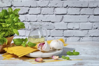 Basil, spaghetti, olive oil and garlic on a table in front of a white brick wall