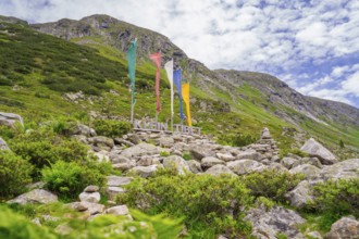 Landscape in the mountains with colourful flags, a sign and green vegetation, framed by rocks,