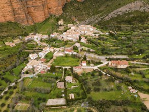 Aerial view of a picturesque village surrounded by green hills and striking orange rocks, aerial