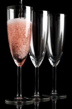 Three champagne glasses in front of a black background, first glass is filled with champagne