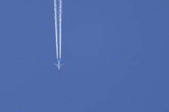 Airbus jet passenger aircraft flying in a blue sky with a vapor trail or contrail behind, England,