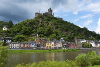 Image of a castle on a green hill with colourful, historic buildings along a river, cloudy sky,