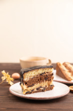 Chocolate biscuit cake with caramel cream, cup of coffee on brown wooden background. side view,