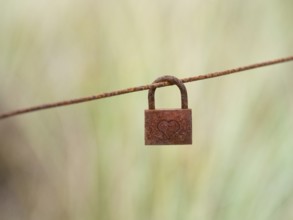 A Rusty Lock, with a heart inscribed upon it, hanging on a fence wire, island of Texel, Holland