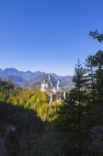 Neuschwanstein Castle in the midst of autumn forests with a majestic mountain backdrop under a