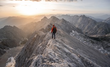 Mountaineer with helmet on a narrow rocky ridge at sunrise, crossing the Jubiläumsgrat, view of